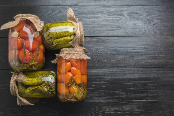 Canned vegetables cucumber and tomato in glass jars on wooden dark board. Space for text. View from above. Homemade harvest fall preparations. Homework and traditions.