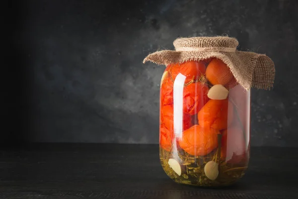 Homemade marinated tomatoes. Canned vegetables in glass jars on wooden board. Space for text.