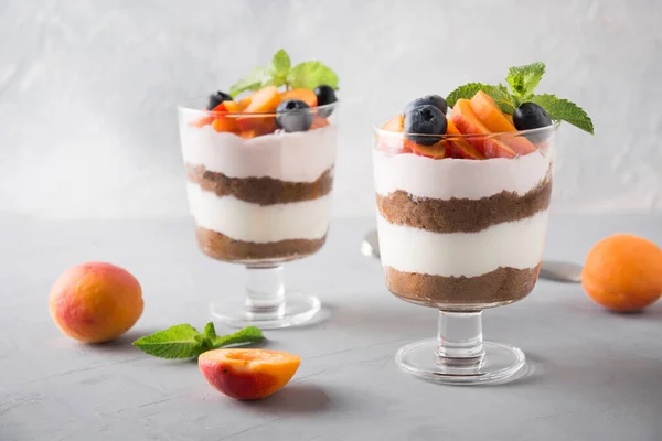 Bagatela de albaricoque, galleta de chocolate, postre en capas con bayas frescas y queso crema suave en gris . — Foto de Stock