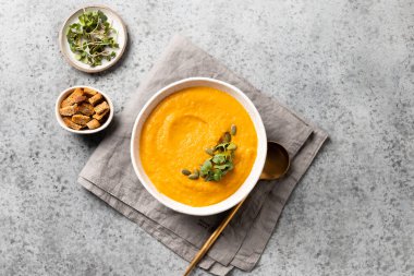 Krakerli balkabağı çorbası. Gri taşlı arka planda küçük yeşillikler. Yukarıdan görüntüle.