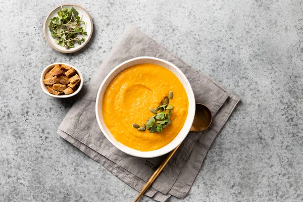 Krakerli balkabağı çorbası. Gri taşlı arka planda küçük yeşillikler. Yukarıdan görüntüle.