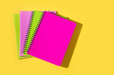 Parlak okul malzemeleri, sarı arka planda not defterleri. Üst manzara, düz yatış. Boşluğu kopyala.