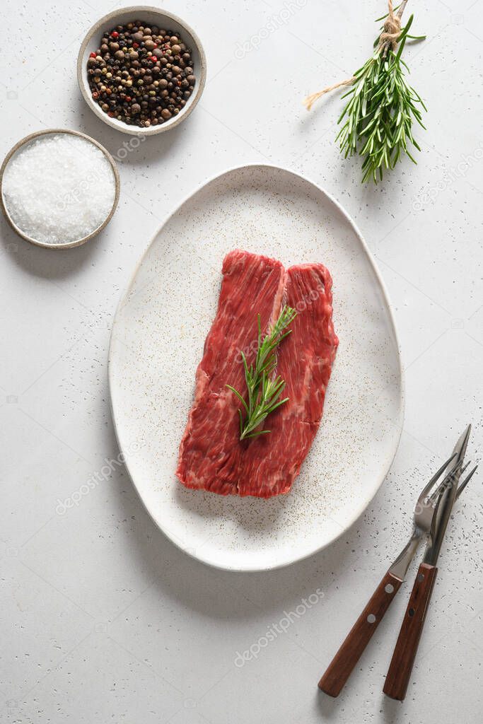 Raw ribeye steak with rosemary on white .