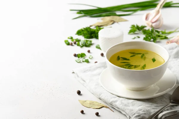 Bouillon de poulet avec oignon vert dans un bol blanc sur une table blanche. Espace de copie. — Photo