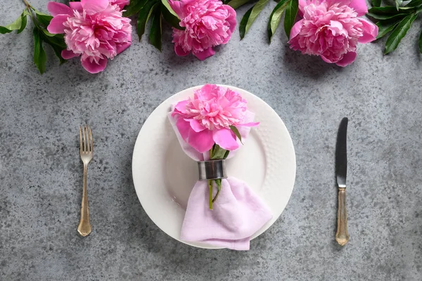 Elegante Tischdekoration mit rosa Pfingstrose, weißem Geschirr, Tafelbesteck auf grau. Ansicht von oben. — Stockfoto