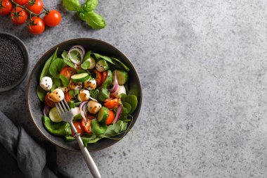 Ispanaklı sağlıklı salata, kiraz domatesleri, fesleğen, soğan ve gri taşlı arka planda Mozzarella. Vejetaryen yemeği. Üst Manzara. Boşluğu kopyala.