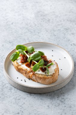 Gri arkaplanda kurutulmuş domatesli ve turp mikroyeşili bir sandviç..