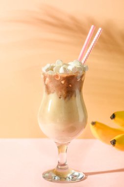 Çikolatalı ve muzlu milkshake. Pembe ve bej kağıtlı gölgeli. Dikey format. Temiz yemek..