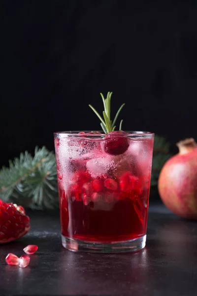 Pomegranate Christmas cocktail with rosemary, champagne, club soda on black table. Close up. Vertical format.