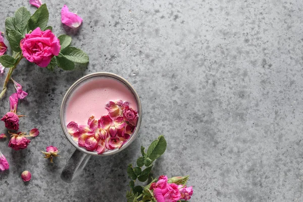 Rose moon milk in grey cup and rose petals on grey. Top view.