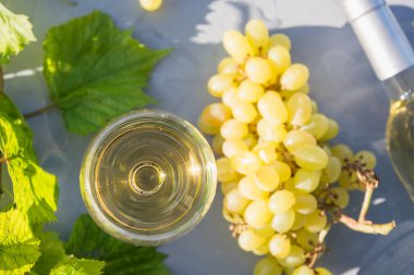 Şarap kadehinde beyaz şarap, güneşli ışıkta gri masada olgun üzüm. Kapatın. Açık havada..