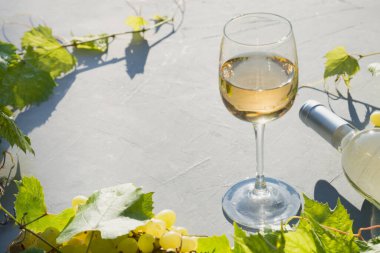 Gri masadaki güneşli yaz güneşinde beyaz şarap ve üzümlü cam sınırı. Kapatın. Açık havada..