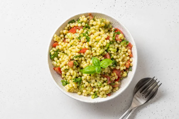 Pasta ptitim con verduras decoradas con hojas de albahaca sobre blanco. Vista superior. Espacio para texto. — Foto de Stock