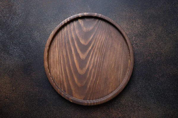 Wooden round cutting board on dark brown kitchen background. Top view flat lay. — Stock Photo, Image