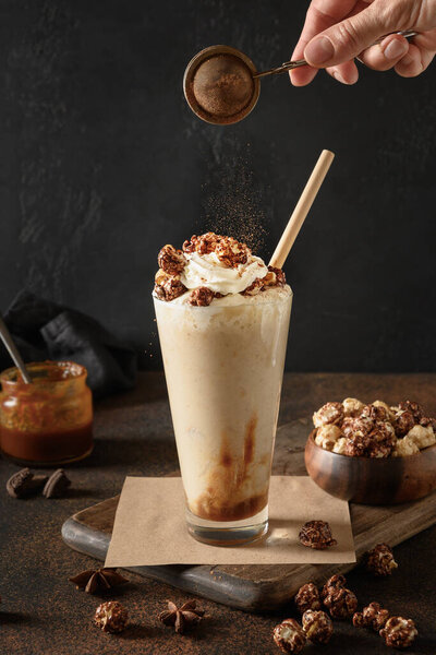 Banana milkshake garnish caramel and whipped cream sprinkled cacao powder on dark. 