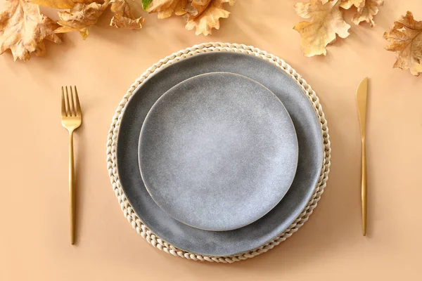 Fall table setting with autumn oak leaves and golden cutlery on beige background. View from above.