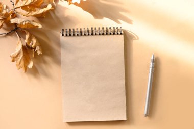 Boş, eskiz defterinin sonbahar kompozisyonu ve bej üzerine altın kuru meşe yaprakları. Güneşli gölgeli bir şablon oluşturun. Uzayı kopyala Yukarıdan görüntüle.