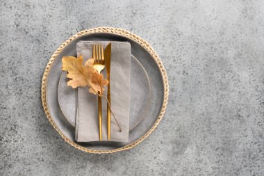Gri masaya kuru meşe yaprağı ve altın çatal bıçak döşeme seti. Yukarıdan görüntüle.