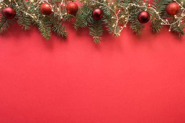 Різдвяна рамка з вічнозеленими гілками, гірлянда, червоні кульки, подарунок на червоному — стокове фото