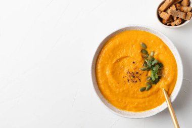 Balkabağı çorbasını kremalı garnitür mikro yeşillikleriyle beyaz arka planda fotokopi alanı ile doldurun. Yukarıdan görüntüle.