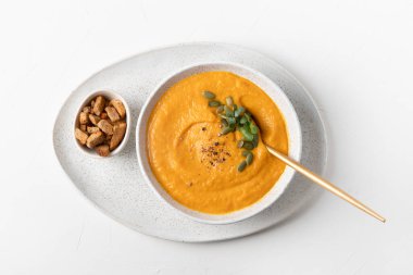 Sonbahar balkabağı çorbası beyaz masada kraker ve mikroyeşillikler servis ediliyordu. Yukarıdan görüntüle.