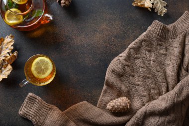 Kahverengi arka planda sıcak çay, dökülen yapraklar ve süveter ile sonbahar kompozisyonu. Yukarıdan kopyalama alanı ile görüntüle.