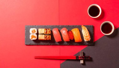 Soya sosu, turşu turşusu zencefil ve wasabi gibi geleneksel eşlikçilerle servis edilen rafine bir suşi seçimi, zarif bir görsel efekt için zıt kırmızı ve siyah bir zemin üzerine yerleştirilmiş yemek çubukları ile.