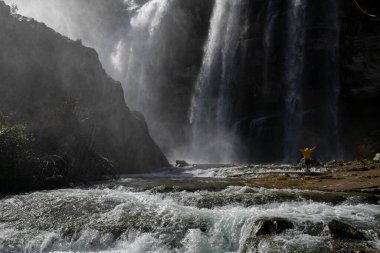 Türkiye 'deki Tortum şelalesinde dinlenen sarı ceketli bir turist. Erzurum 'daki Tortum Şelalesi' nde elleri açık bir kayanın üzerinde duran genç bir gezgin.