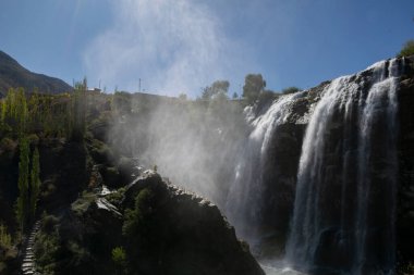 Türkiye 'deki Tortum şelalesinde dinlenen sarı ceketli bir turist. Erzurum 'daki Tortum Şelalesi' nde elleri açık bir kayanın üzerinde duran genç bir gezgin.