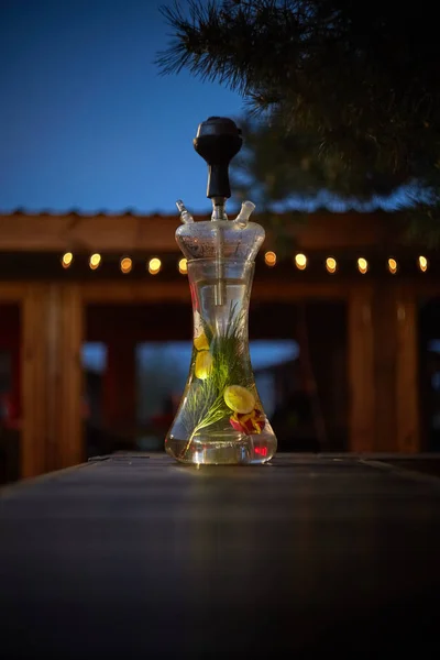 Modern Hookah for tobacco smoking made of metal, glass and plastic on wooden table.The background-summer sunny garden. Selective focus.