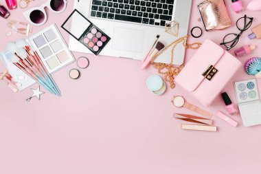 Fashion blogger workspace with laptop and female accessory, cosmetics products on pale pink table. flat lay, top view clipart