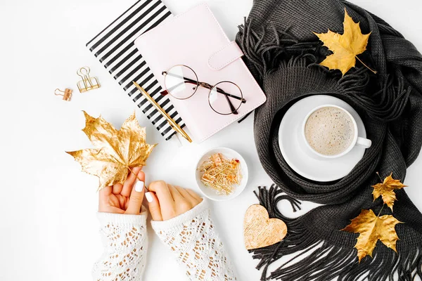 Woman holding an empty card. Workspace with   coffee cup wrapped in scarf, golden clips, glasses. Stylish office desk. Autumn or Winter concept.  Flat lay, top view