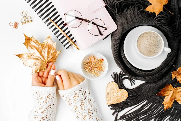 Woman holding an empty card. Workspace with   coffee cup wrapped in scarf, golden clips, glasses. Stylish office desk. Autumn or Winter concept.  Flat lay, top view