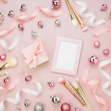 Noel baubles, kurdeleler, makyaj fırçaları, hediye ve pastel pembe bir arka plan üzerinde boş çerçeve