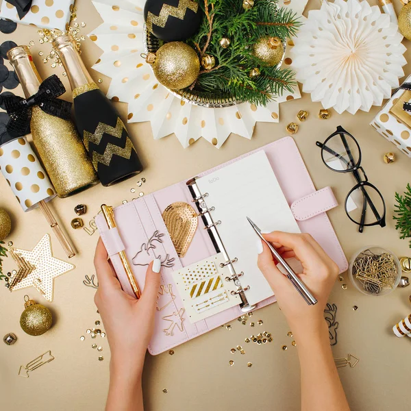 Female hands write in planner or notebook. Christmas decoration background in golden and black colors. Flat lay, top view