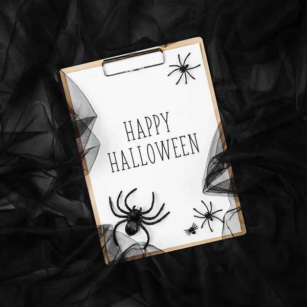 happy halloween card on clipboard with Spiders and web over black background