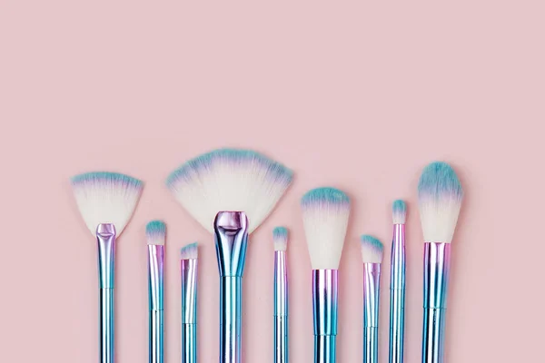 Fashion holographic colored makeup brushes on a pastel pink background. Flat lay, top view