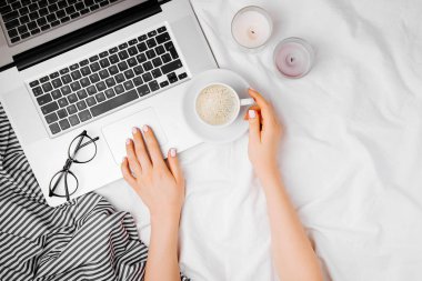 kahve fincanı ile dizüstü bilgisayar, eller üstten görünüm yatakta