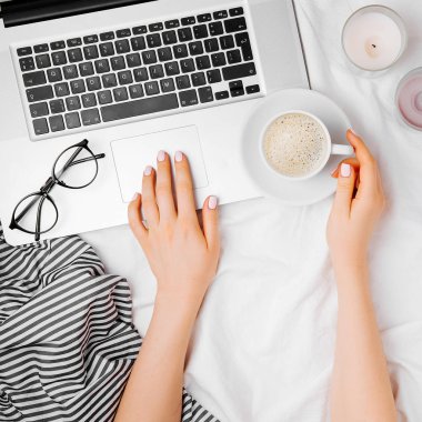 kahve fincanı ile dizüstü bilgisayar, eller üstten görünüm yatakta