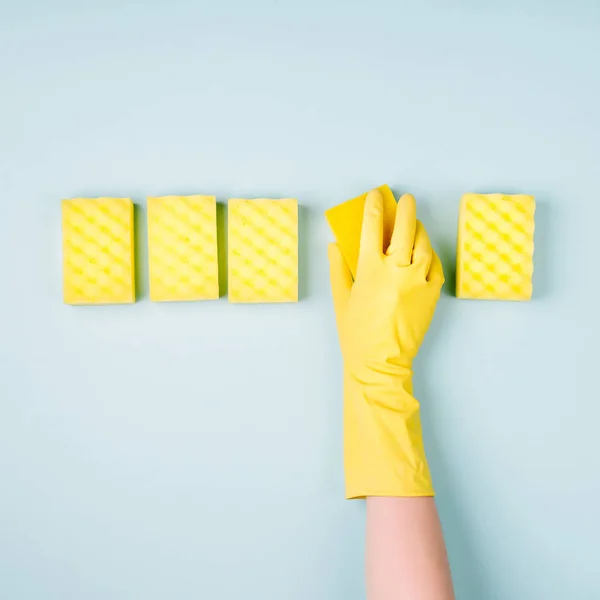 top view of cleaner hand in glove with sponges on blue background