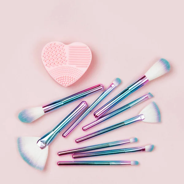 Fashion holographic colored makeup brushes with Brush Cleansing Pad on a pastel pink background. Flat lay, top view