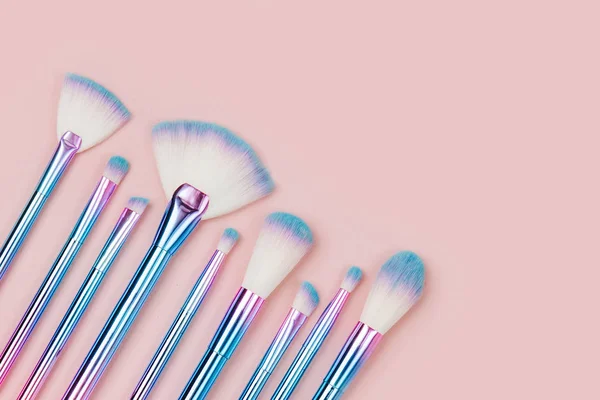 Fashion holographic colored makeup brushes on a pastel pink background. Flat lay, top view