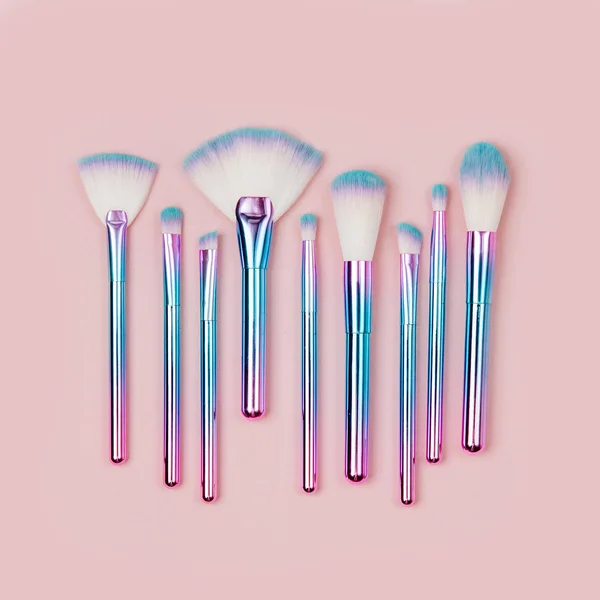 Fashion holographic colored makeup brushes on a pastel pink background. Flat lay, top view