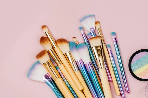 Fashion holographic colored makeup brushes with eye shadow and powder  on a pastel pink background. Flat lay, top view