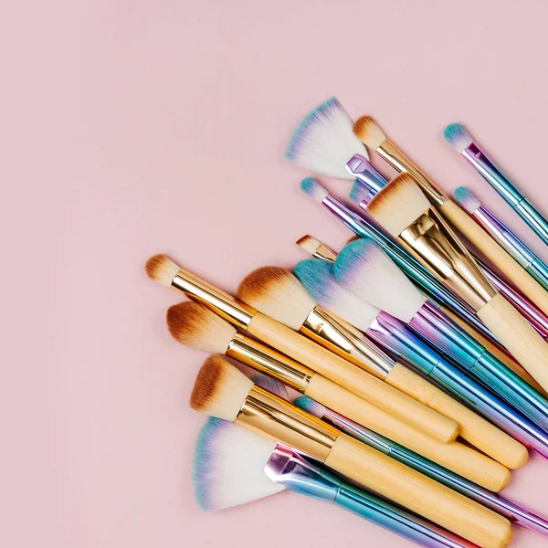 Fashion holographic colored makeup brushes with eye shadow and powder  on a pastel pink background. Flat lay, top view