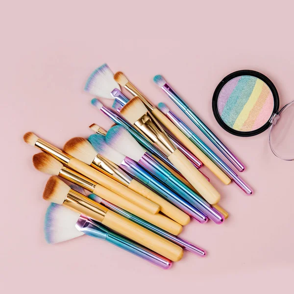 Fashion holographic colored makeup brushes with eye shadow and powder  on a pastel pink background. Flat lay, top view