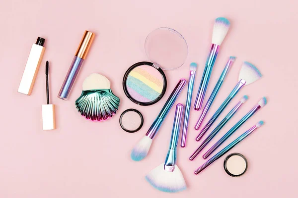 Fashion holographic colored makeup brushes with eye shadow and powder on pastel pink background
