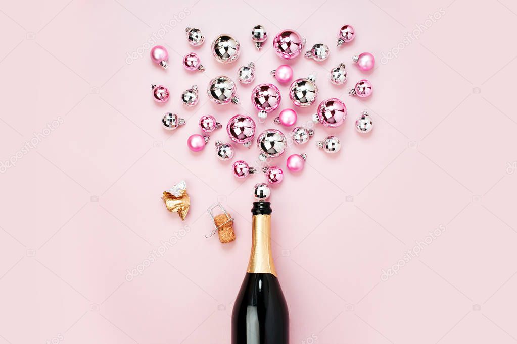 top view of champagne bottle with christmas baubles on pale pink background