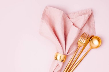 Altın çatal bıçak takımı ve pastel arka plan üzerinde soluk pembe peçete. Düz yatıyordu, en iyi görünümü