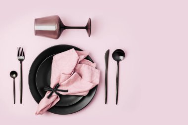 Çatal bıçak takımı, soluk pembe peçete, siyah plakalar ve pastel arka plan üzerinde şarap kadehi ile Festival tablo ayarı. Düz yatıyordu, en iyi görünümü